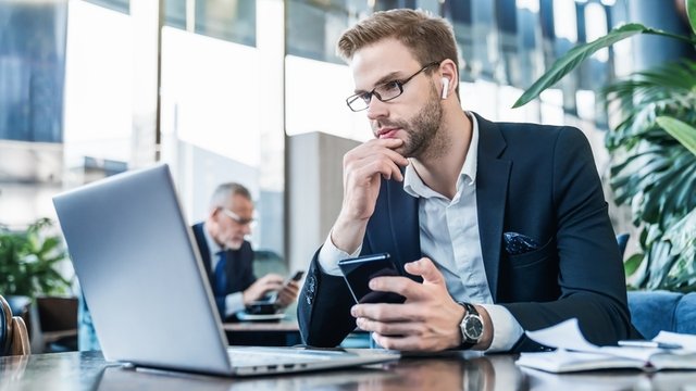trader mira atento la pantalla de un ordenador portátil, mientras mantiene una conversación por el teléfono móvil