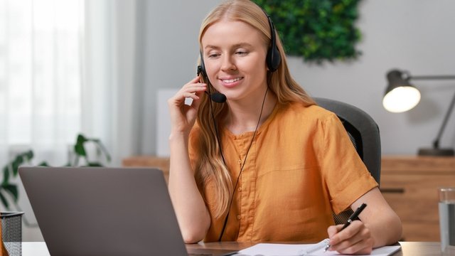 traductora lleva puestos unos auriculares mientras toma notas frente a su ordenador portátil