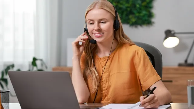 traductora lleva puestos unos auriculares mientras toma notas frente a su ordenador portátil