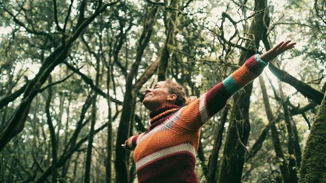 mujer sonriente y con los brazos abiertos en mitad de un bosque