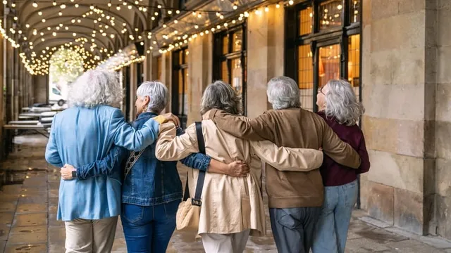 Un grupo diverso de personas mayores, caminando brazo a brazo a lo largo de una arcada iluminada, compartiendo un momento de estilo de vida retirado