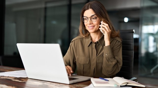 mujer sentada frente a un ordenador portátil realizando una llamada telefónica