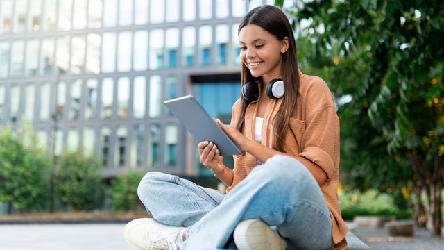 estudiante usando una tableta en el jardín de un campus universitario