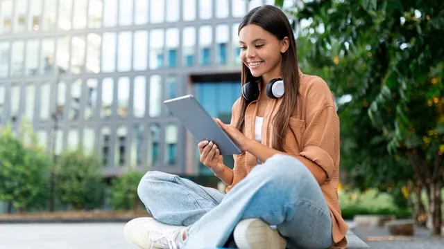 estudiante usando una tableta en el jardín de un campus universitario